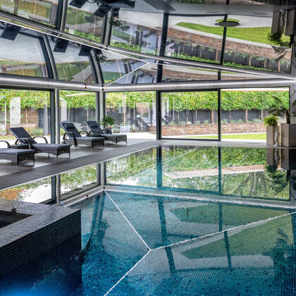 Luxury indoor swimming pool in Cheshire featuring a high-gloss black stretch ceiling and seamless porcelain tiled surround and floor-to-ceiling architectural glazing overlooking a Cheshire garden.