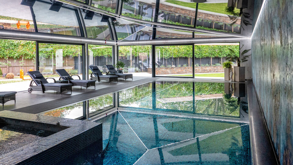 Luxury indoor swimming pool in Cheshire featuring a high-gloss black stretch ceiling and seamless porcelain tiled surround and floor-to-ceiling architectural glazing overlooking a Cheshire garden.
