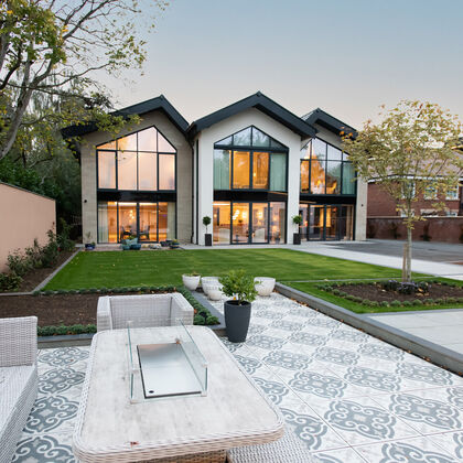Evening view of a bespoke Cheshire residence with a triple-gable rear elevation and architectural floor to ceiling glazing with stone cladding