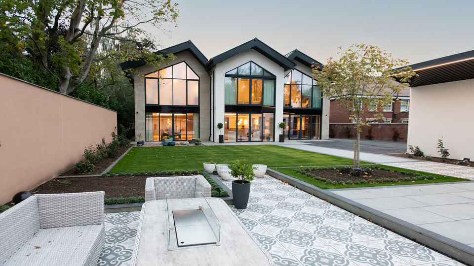 Evening view of a bespoke Cheshire residence with a triple-gable rear elevation and architectural floor to ceiling glazing with stone cladding