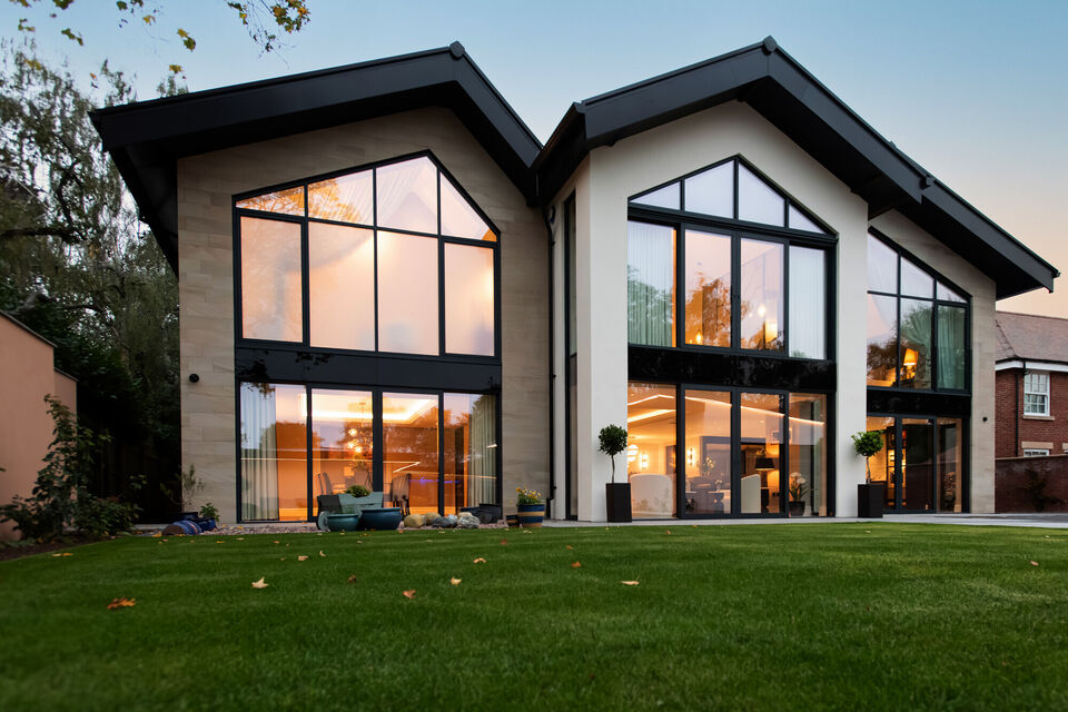 Evening view of a bespoke Cheshire residence with a triple-gable rear elevation and architectural floor to ceiling glazing with stone cladding