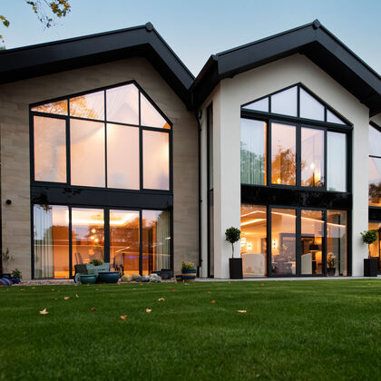 Evening view of a bespoke Cheshire residence with a triple-gable rear elevation and architectural floor to ceiling glazing with stone cladding