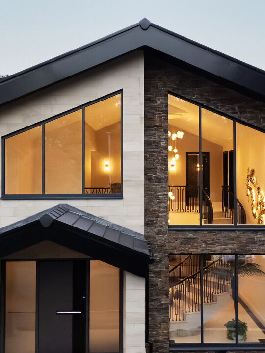 Front elevation of a bespoke Cheshire residence featuring light ashlar stone masonry, dark grey window frames, and a modern gabled entrance, spiral stair.