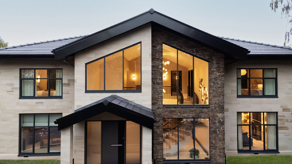 Front elevation of a bespoke Cheshire residence featuring light ashlar stone masonry, dark grey window frames, and a modern gabled entrance, spiral stair.