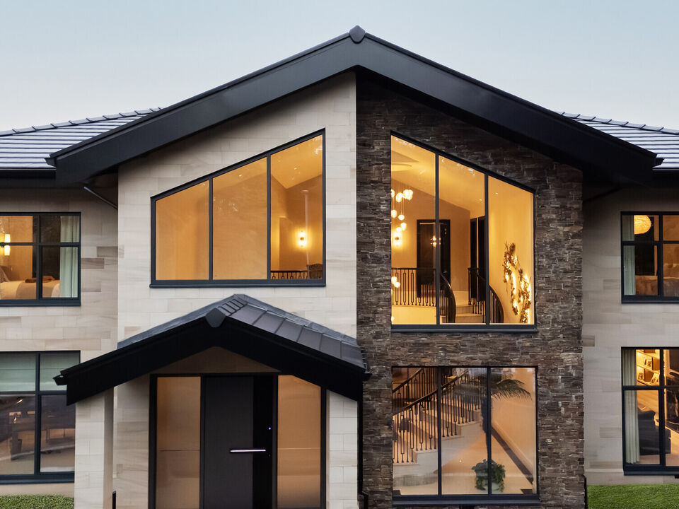 Front elevation of a bespoke Cheshire residence featuring light ashlar stone masonry, dark grey window frames, and a modern gabled entrance, spiral stair.
