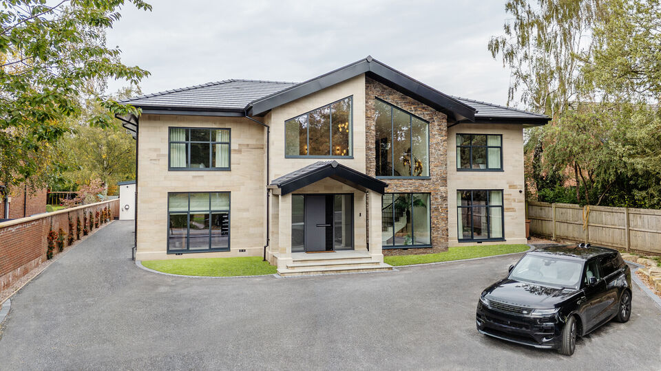 Front elevation of a bespoke Cheshire residence featuring light ashlar stone masonry, dark grey window frames, and a modern gabled entrance.