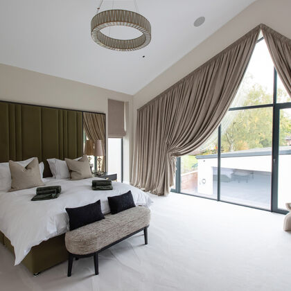 Luxury contemporary bedroom with vaulted ceiling, bespoke headboard and full-height glazing