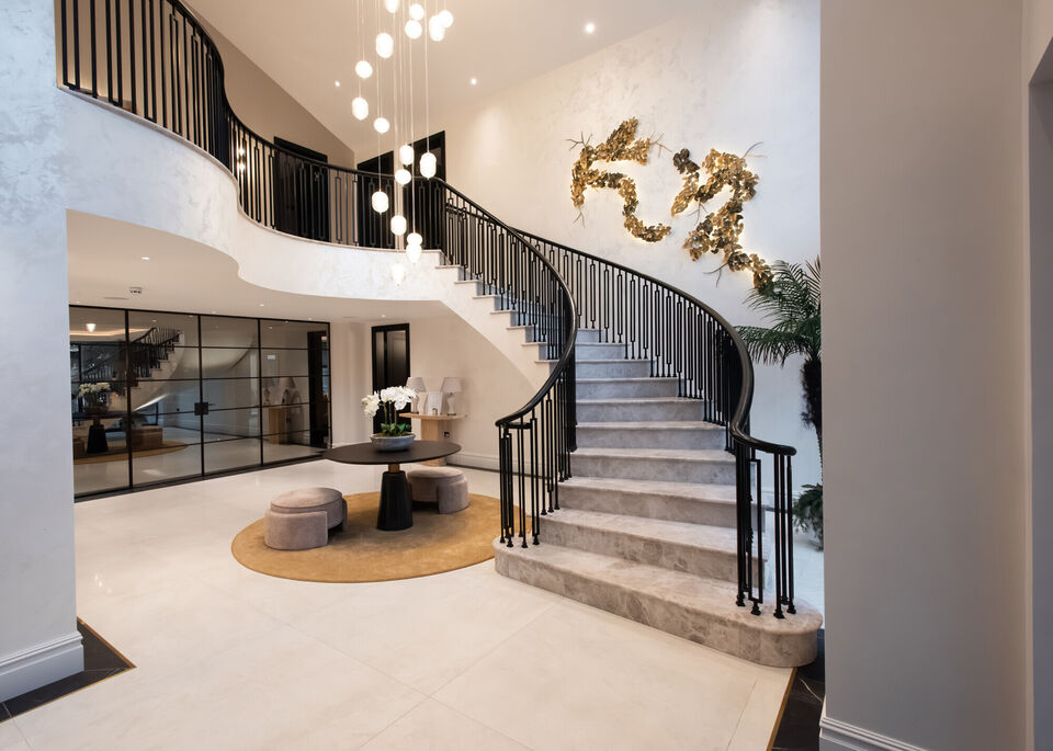 Luxury entrance hall with sweeping curved staircase, double-height space and feature lighting, art deco railings, stone floors