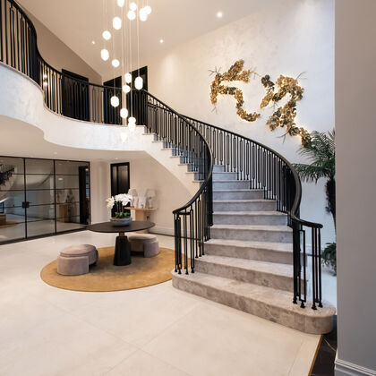 Luxury entrance hall with sweeping curved staircase, double-height space and feature lighting, art deco railings, stone floors