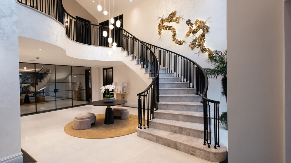 Luxury entrance hall with sweeping curved staircase, double-height space and feature lighting, art deco railings, stone floors