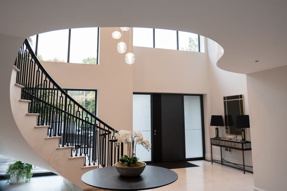 Luxury double-height entrance hall with curved staircase, feature glazing and pendant lighting