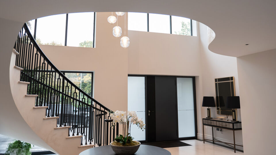 Luxury double-height entrance hall with curved staircase, feature glazing and pendant lighting