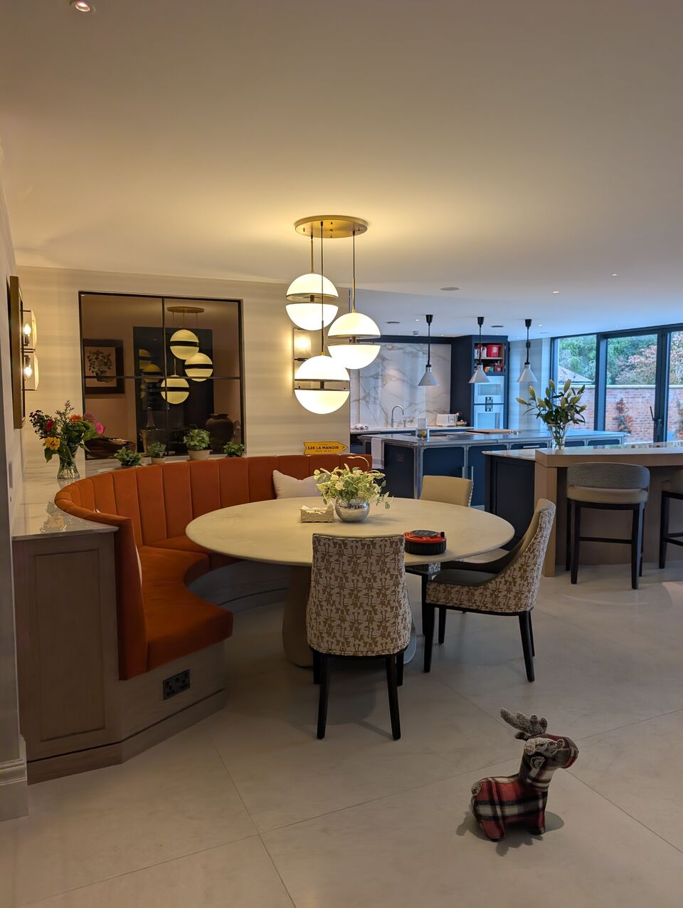Luxury open-plan dining area with bespoke banquette seating, statement pendant lights and kitchen beyond