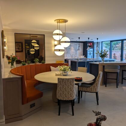 Luxury open-plan dining area with bespoke banquette seating, statement pendant lights and kitchen beyond
